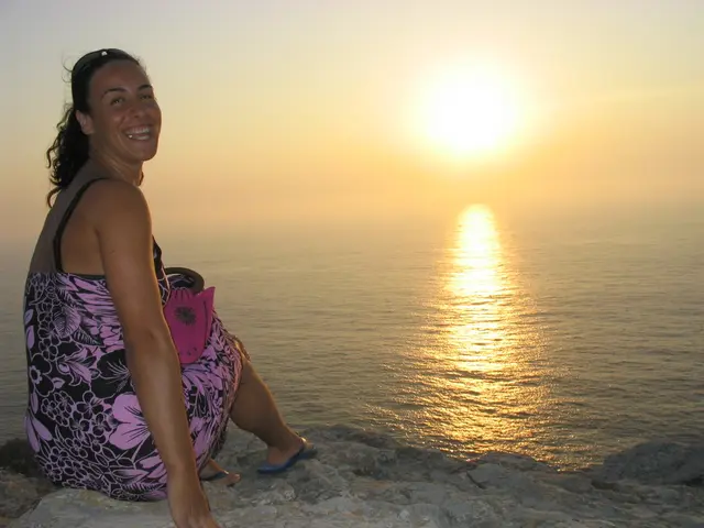 In this image I can see a woman sitting on the left. There is water in the center and sun in the...