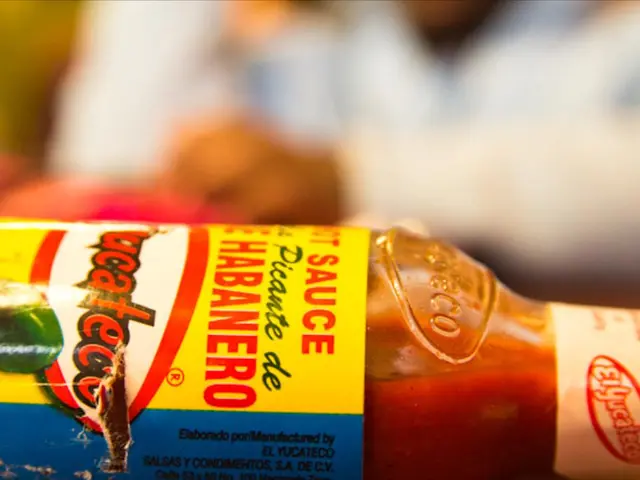 In this image,There is a hot chilli sauce bottle, And in the background there is some person...