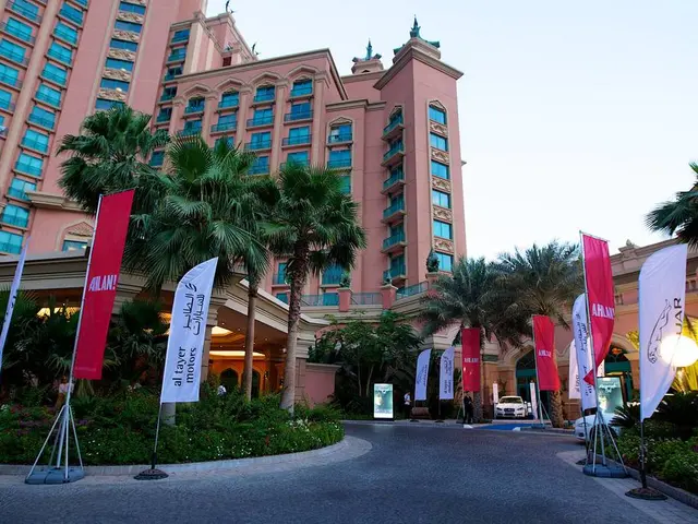 In this picture we can see a few advertising flags. There are plants, flowers, vehicles, a few...