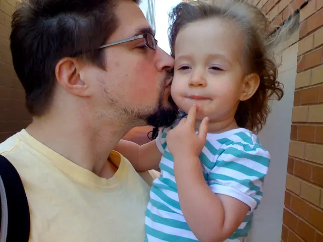 In the front of the image I can see a person is kissing a kid. On the left side of the image and...