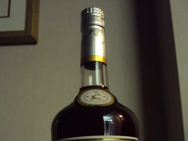 In this image, there is a bottle. This bottle has a label and contains some text. There is wall...