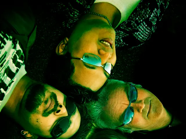 In this image we can see group of people lying on ground. Some persons are wearing goggles. In the...