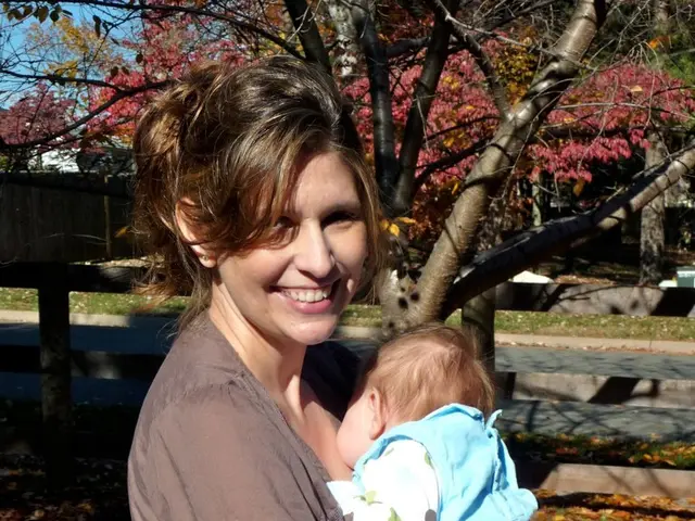 This is the woman standing and smiling. She is carrying a baby in her hands. I can see the dried...